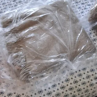 Sale Photo Thumbnail #46: Beige fringed wool or cashmere throw blanket, folded and sealed inside clear plastic packaging.