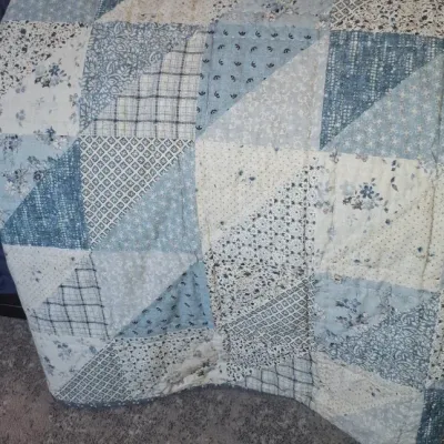 Sale Photo Thumbnail #37: Handmade patchwork quilt featuring geometric half-square triangle patterns in soft blue, gray, and cream floral and plaid fabrics.