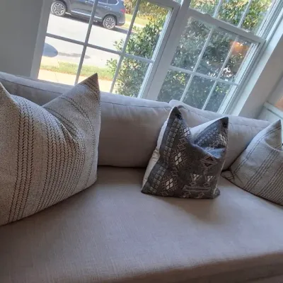 Sale Photo Thumbnail #2: Contemporary beige upholstered daybed sofa, styled with a assortment of patterned throw pillows and positioned next to a window nook.