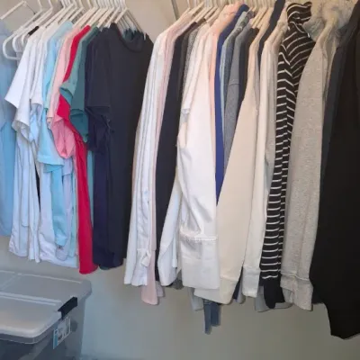Sale Photo Thumbnail #62: Closet hanging rack featuring a variety of casual men's and women's shirts, sweaters, and jackets alongside clear plastic storage bins.