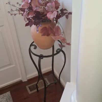 Sale Photo Thumbnail #56: Faux artificial plant arrangement in a terracotta-style urn, displayed on a black wrought iron plant stand.