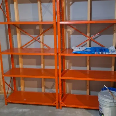 Sale Photo Thumbnail #66: Pair of heavy-duty orange steel five-tier industrial shelving units set up against an unfinished basement wall.