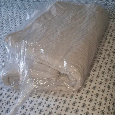 Sale Photo Thumbnail #52: Folded beige quilted blanket wrapped in clear plastic, resting on a bed with a floral patterned coverlet.