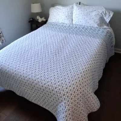 Sale Photo Thumbnail #48: Bedroom setup featuring a fully made bed with floral patterned bedding and pillow shams, positioned next to a small dark wood nightstand.