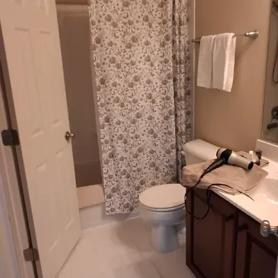 Sale Photo Thumbnail #44: Full bathroom featuring a dark wood vanity, white toilet, patterned shower curtain, and plush bath runner.