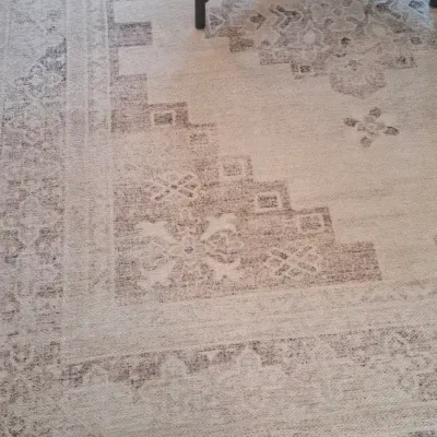 Sale Photo Thumbnail #4: Large area rug featuring a muted cream and grey traditional medallion pattern with distressed details, partially underneath a round wooden coffee table with a black metal base.