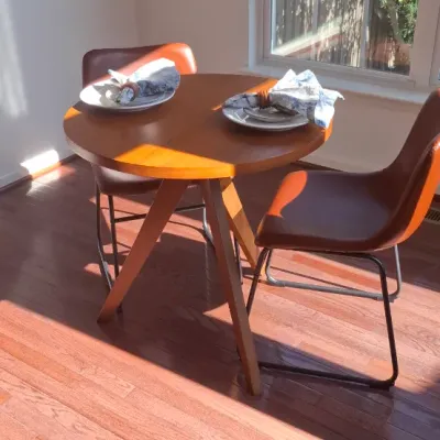 Sale Photo Thumbnail #10: Round mid-century style wooden dining table with angled legs, paired with two cognac leatherette chairs featuring black metal sled bases.