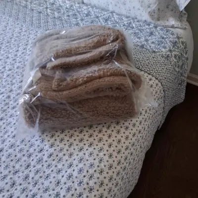 Sale Photo Thumbnail #47: Tan plush fleece blanket packaged in a clear plastic bag, resting on a bed made with floral patterned linens.