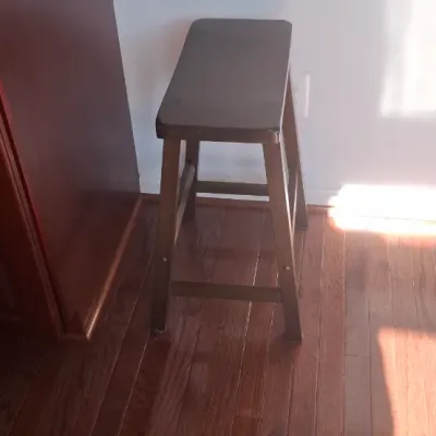 Sale Photo Thumbnail #9: Dark brown wooden saddle seat bar stool standing next to a kitchen island with granite countertop.