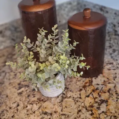 Sale Photo Thumbnail #72: Set of two vintage mid-century hammered dark amber glass canisters with wooden lids, displayed alongside a small potted artificial plant.