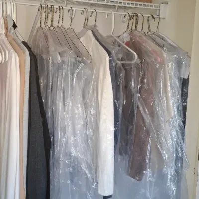 Sale Photo Thumbnail #61: Closet filled with women's hanging clothing, many protected in plastic dry cleaning bags, under an upper wire shelf holding a small lamp and a boxed Levoit humidifier.