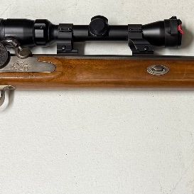 Sale Photo Thumbnail #12: Percussion lock black powder muzzleloader rifle with a wooden stock, double set triggers, and a mounted modern optic scope.