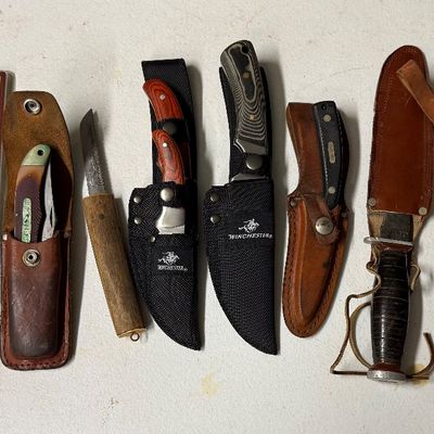 Sale Photo Thumbnail #6: Collection of fixed-blade and folding hunting knives, including Winchester gift set, Marttiini Scandinavian knives with leather sheaths, and vintage military-style leather sheath knives.