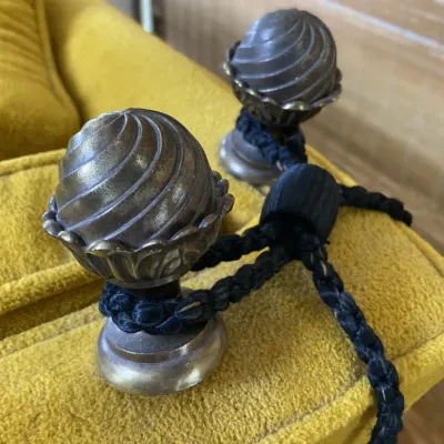 Sale Photo Thumbnail #134: Vintage ornate metal finials with dark braided trim resting on mustard yellow upholstery.