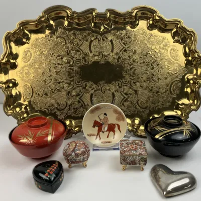 Sale Photo Thumbnail #200: Collection of decorative Asian tableware and trinket boxes, featuring a large ornate brass serving tray, Japanese lacquer lidded bowls, hand-painted porcelain boxes, and a silver-tone heart-shaped dish.