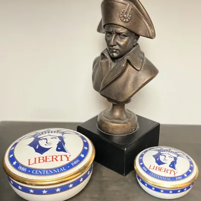 Sale Photo Thumbnail #107: Bronze-tone bust of Napoleon Bonaparte on a black pedestal, paired with two ceramic Statue of Liberty 1886–1986 Centennial trinket boxes with gold trim.