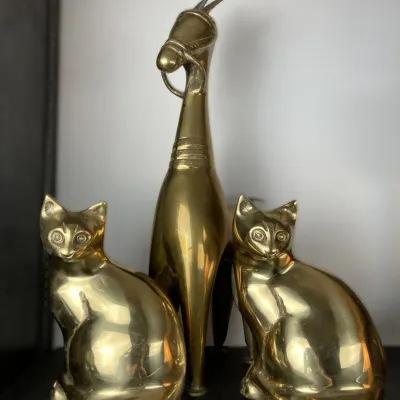 Sale Photo Thumbnail #78: Vintage polished brass animal figurines, including a pair of seated cat statues flanking a tall stylized horse sculpture.