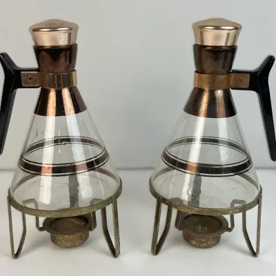 Sale Photo Thumbnail #42: Pair of mid-century modern glass coffee carafes featuring copper-tone accents, black handles, and matching metal warmer stands with candle holders.
