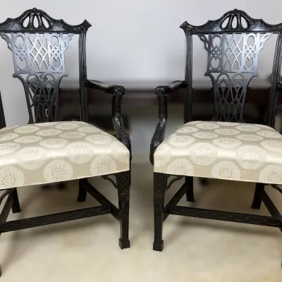 Sale Photo Thumbnail #129: Pair of Chippendale-style carved black wood armchairs featuring intricate fretwork backs and cream-colored patterned fabric upholstered seats.