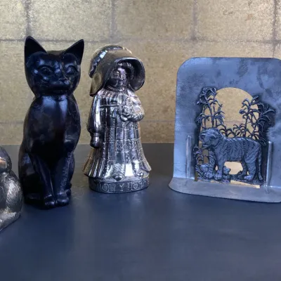 Sale Photo Thumbnail #230: Collection of decorative metal figurines and bookends, including a silver-tone squirrel, black cat statuette, vintage Holly Hobbie figure, and a pair of cut-out tiger bookends.