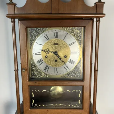 Sale Photo Thumbnail #70: Traditional wooden mantle clock featuring brass finials, a bonnet top with scrollwork, and an ornate silver and gold-tone dial face.
