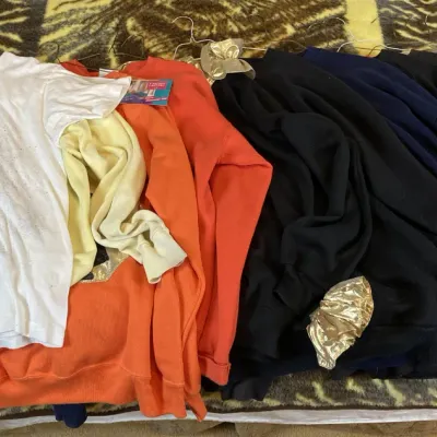 Sale Photo Thumbnail #151: Collection of vintage casual shirts and sweatshirts laid out on a patterned blanket, including a Halloween-themed ghost graphic tee and various solid-colored long-sleeve tops.