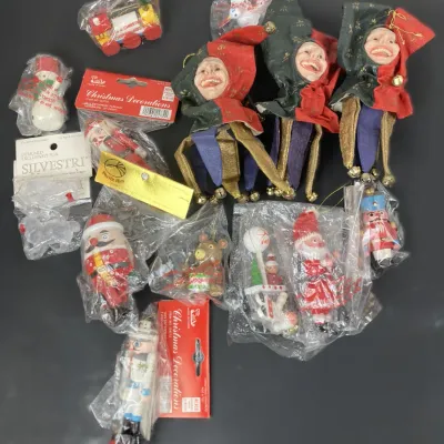 Sale Photo Thumbnail #211: Collection of vintage Christmas ornaments in original plastic packaging, including jester dolls, mini nutcrackers, a wooden train, and Santa figures.