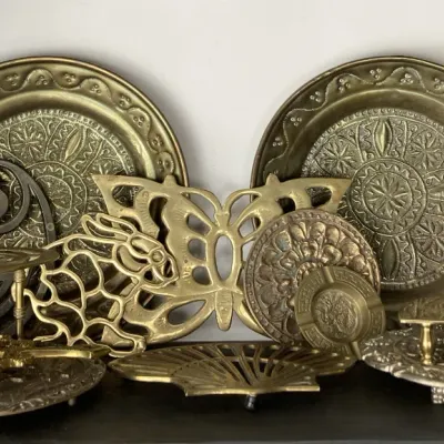 Sale Photo Thumbnail #90: Collection of vintage brass decorative items, including embossed wall plates, trivets shaped like butterflies and rabbits, and small footed stands.