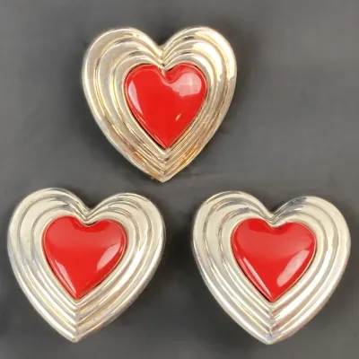 Sale Photo Thumbnail #23: Set of three vintage heart-shaped brooches featuring layered silver-tone concentric frames surrounding glossy red enamel centers.