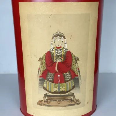 Sale Photo Thumbnail #92: Vintage red metal trash can featuring a printed illustration of an Asian ancestor portrait, showing minor wear and surface discoloration.