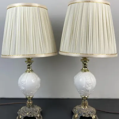 Sale Photo Thumbnail #102: Pair of vintage table lamps featuring ornate brass bases, white milk glass center urns with raised floral motifs, and pleated cream shades.