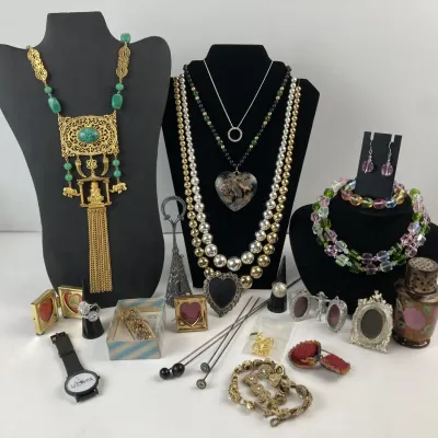 Sale Photo Thumbnail #199: Eclectic collection of vintage costume jewelry and trinkets, including beaded necklaces, ornate pendant necklaces on displays, small picture frames, and a watch.