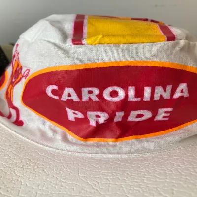 Sale Photo Thumbnail #165: Vintage white promotional bucket-style sun visor featuring a red and yellow 'Carolina Pride' logo, in good used condition.