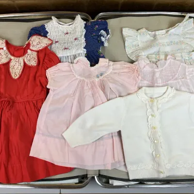 Sale Photo Thumbnail #245: Collection of vintage children's clothing including smocked dresses and a knit cardigan, neatly displayed inside an open hard-shell suitcase.