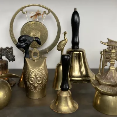 Sale Photo Thumbnail #88: Collection of decorative vintage brass bells and tabletop gongs, featuring stylized owl, bird, Liberty Bell, and Asian-inspired architectural designs.