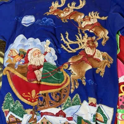 Sale Photo Thumbnail #155: Vintage royal blue holiday sweatshirt featuring a detailed graphic print of Santa in his sleigh with flying reindeer, embellished with glitter accents.