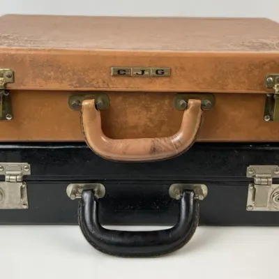 Sale Photo Thumbnail #232: Pair of vintage hard shell leather briefcases, including a tan model personalized with 'CJG' initials stacked on top of a black model, both featuring metal latches.