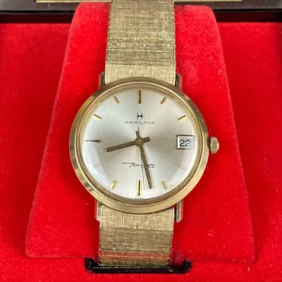 Sale Photo Thumbnail #166: Vintage Hamilton Thin-o-matic gold-tone wristwatch featuring a textured mesh metal strap and a date display, displayed inside its original presentation box with red velvet lining.