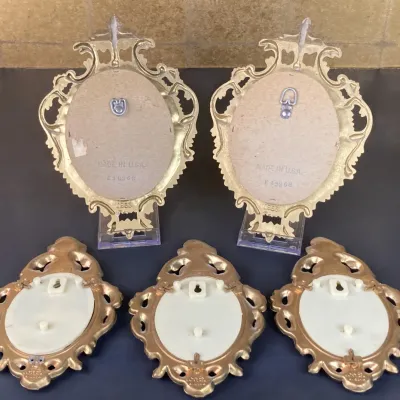 Sale Photo Thumbnail #168: Set of five vintage ornate gold-tone wall plaques shown from the reverse, featuring elaborate Rococo-style scrollwork borders.