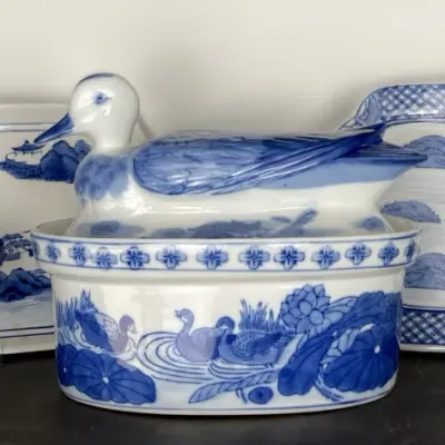 Sale Photo Thumbnail #75: Collection of blue and white Asian-style porcelain decor including a duck-form tureen, butterfly-shaped teapot, rectangular platters, and a small handled basket.