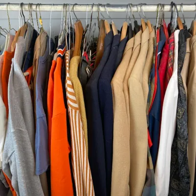 Sale Photo Thumbnail #156: Selection of vintage men's and women's clothing hanging on a closet rod, including jackets, sweaters, and shirts in various colors.
