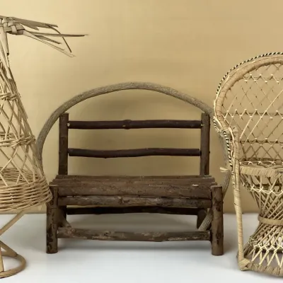 Sale Photo Thumbnail #144: Collection of miniature rustic and wicker furniture, including a wicker peacock chair, a twig bench with an arched handle, and a tall woven wicker plant stand.