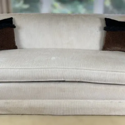 Sale Photo Thumbnail #84: Off-white corduroy upholstered sofa featuring flared arms, turn-of-the-century style wooden finial accents on the frame, and two contrasting throw pillows.