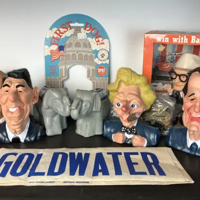 Sale Photo Thumbnail #99: Collection of vintage political memorabilia and caricature novelty items, including vinyl busts of Reagan, Gorbachev, and Clinton, alongside Barry Goldwater campaign collectibles.