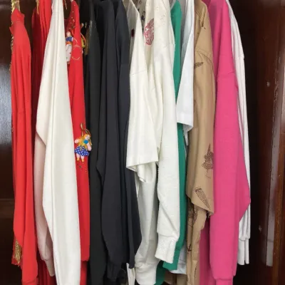 Sale Photo Thumbnail #150: Collection of vintage women's tops and sweaters hanging in a wooden closet, including embellished Christmas sweaters and casual sweatshirts from around the 1980s to 1990s.