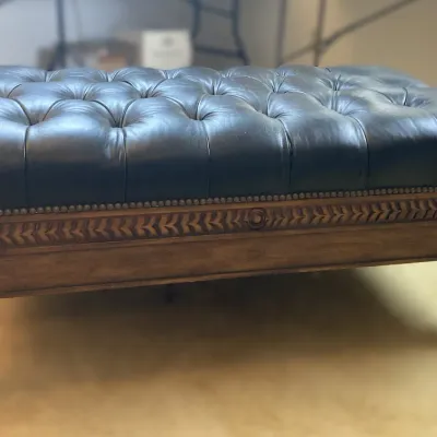 Sale Photo Thumbnail #85: Traditional Chesterfield-style black leather tufted ottoman featuring nailhead trim, a carved wooden apron, and turned legs on brass casters.