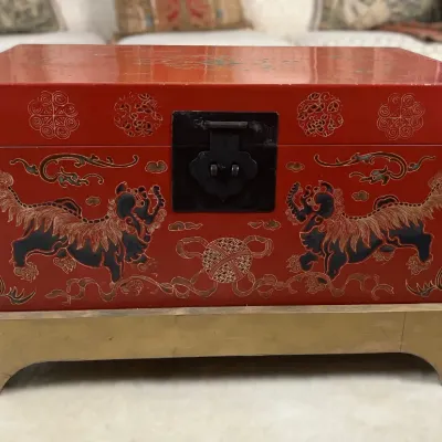 Sale Photo Thumbnail #14: Red lacquered Asian storage trunk decorated with hand-painted foo dogs and gilt detailing, resting on a wooden base.