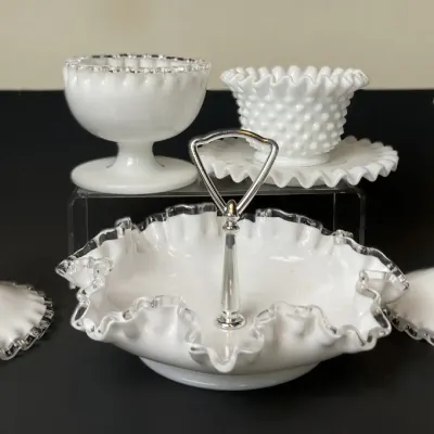 Sale Photo Thumbnail #25: Collection of Fenton white milk glass pieces, including silver crest ruffle-edge candlesticks, a handle dish, a hobnail bowl, and a pedestal bowl.