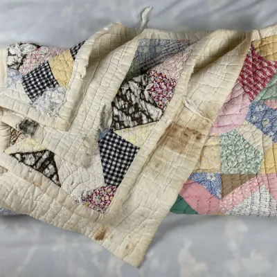 Sale Photo Thumbnail #174: Vintage handmade patchwork quilt featuring colorful geometric patterns, showing visible wear and staining along the edges.