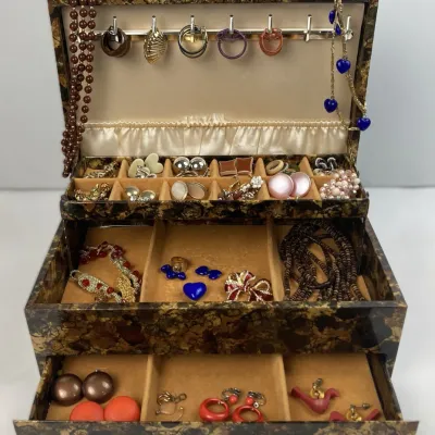 Sale Photo Thumbnail #198: Vintage marbled brown and gold multi-tier jewelry box filled with an assortment of costume jewelry, including clip-on earrings, brooches, and beaded necklaces.